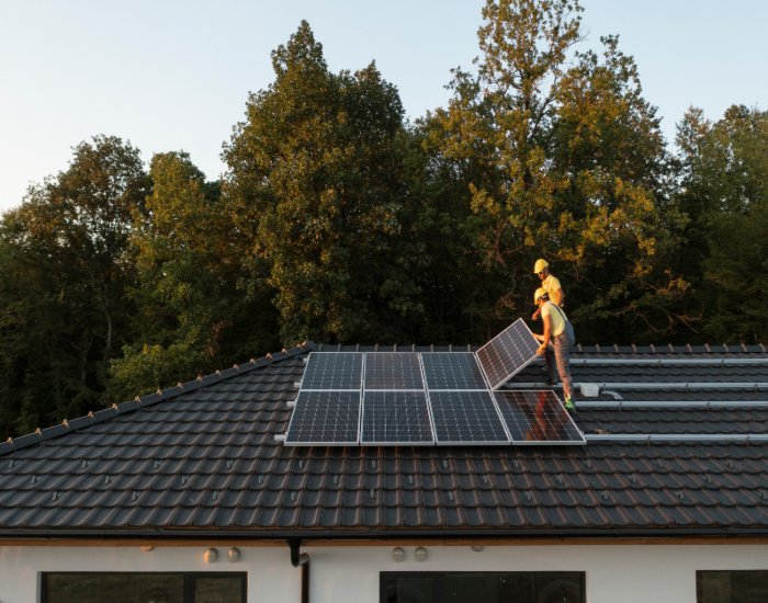 Two men on a rooftop inspect the installation of solar panels on a residential property